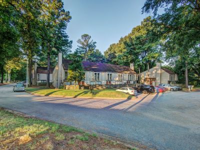 Wide view of the resident parking lot and two-story residential buildings surrounded by trees at Pinewood Manor apartments and townhomes in Memphis.