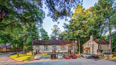 Exterior view of two-story residential townhomes and a paved parking lot shaded by mature pine trees at Pinewood Manor apartments and townhomes in Memphis.