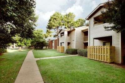 Two-story tan siding residential buildings with private patios and green lawns at Rocky Creek Apartments in Southaven, Mississippi.
