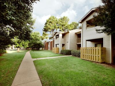 Two-story tan siding residential buildings with private patios and green lawns at Rocky Creek Apartments in Southaven, Mississippi.