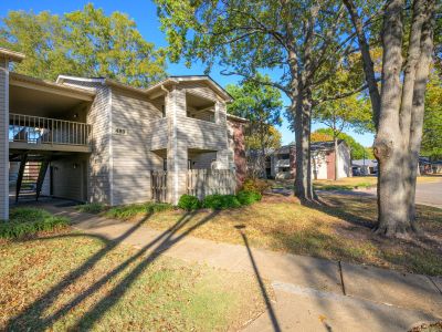 Two-story residential building with tan siding and balconies surrounded by mature trees at Rocky Creek Apartments in Southaven, Mississippi.