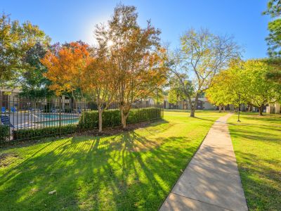 Concrete walking path along a fenced community swimming pool and green lawn at Rocky Creek Apartments in Southaven, Mississippi.