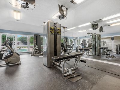 Bright exercise room equipped with stationary bikes, strength training machines, and wall mirrors at Rocky Creek Apartments in Southaven, Mississippi.