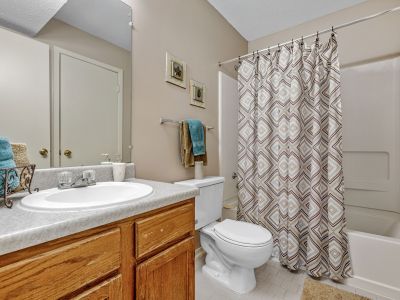 Bathroom featuring an oak vanity, neutral tile floors, and a geometric patterned shower curtain at Rocky Creek Apartments in Southaven, Mississippi.