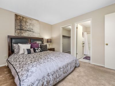 Spacious bedroom with a dark wood headboard, patterned grey bedding, and an attached bathroom at Rocky Creek Apartments in Southaven, Mississippi.