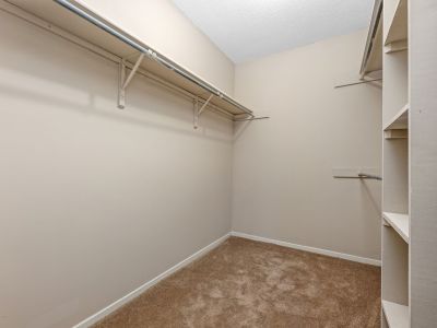 Walk-in closet featuring built-in hanging rods, shelving storage, and tan carpeting at Rocky Creek Apartments in Southaven, Mississippi