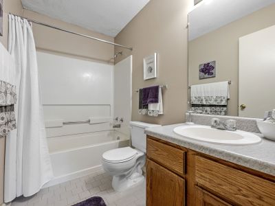 Modern bathroom with an oak vanity, white tub and shower combo, and purple towels at Rocky Creek Apartments in Southaven, Mississippi.
