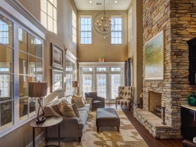 Clubhouse fireplace lounge featuring double-height ceilings, a floor-to-ceiling stone fireplace, and a spherical chandelier at The Signature at Schilling Farms apartments in Collierville.
