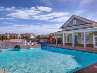 Resort-style outdoor swimming pool with a stone waterfall feature alongside the resident clubhouse pavilion at The Signature at Schilling Farms apartments in Collierville.