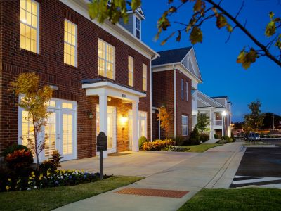Illuminated brick leasing office exterior and sidewalk landscaping at dusk for The Signature at Schilling Farms apartments in Collierville