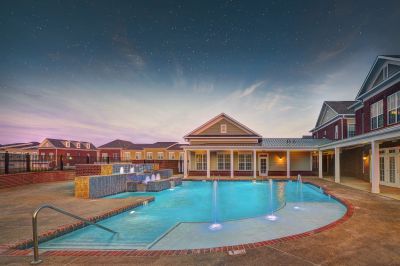 Luxury outdoor swimming pool area with illuminated fountains under a starry twilight sky at The Signature at Schilling Farms apartments in Collierville