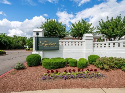 Community entrance monument sign for The Signature at Schilling Farms apartments in Collierville, set against a white brick privacy wall and tidy landscaping