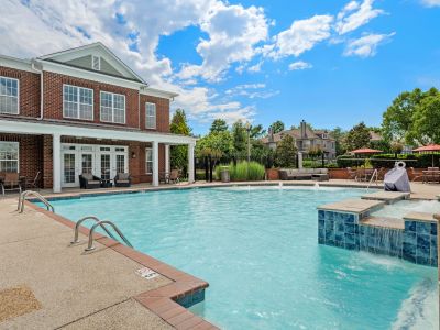 Expansive outdoor swimming pool with tiled water fountain steps bordering a brick resident clubhouse building at The Signature at Schilling Farms apartments in Collierville.