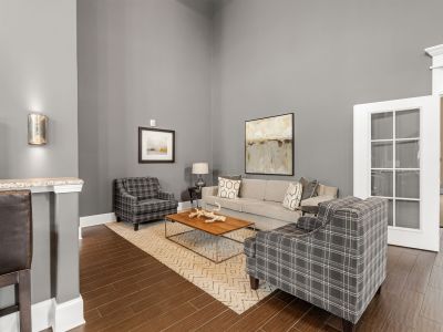 Clubhouse conversation nook featuring grey walls, a neutral sofa, plaid accent chairs, and wood-style flooring at The Signature at Schilling Farms apartments in Collierville.