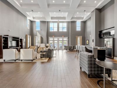 Cavernous resident clubhouse lobby highlighting extensive wood-style flooring, ample seating arrangements, and a kitchen serving bar at The Signature at Schilling Farms apartments in Collierville.