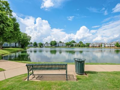 Scenic lakeside walking path with a green metal bench overlooking the community lakefront at The Signature at Schilling Farms apartments in Collierville.