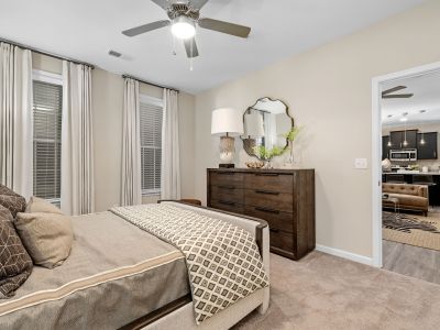 Staged bedroom layout featuring a dark wood dresser, neutral carpet, and patterned bedding at The Signature at Schilling Farms apartments in Collierville near Memphis.