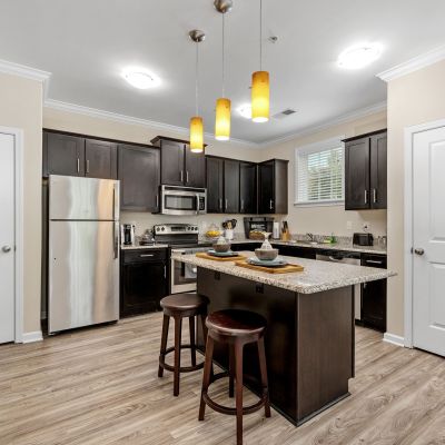 Modern kitchen displaying dark wood cabinets, stainless steel appliances, and a granite-top island bar at The Signature at Schilling Farms apartments in Collierville.
