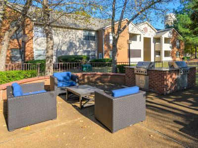 Outdoor grilling area featuring brick barbecue stations and blue cushioned wicker seating at Southcrest Lake Apartments in Southaven