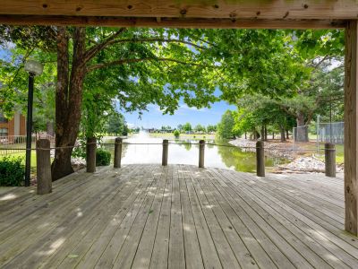 View from under a shaded wooden pergola looking out onto a lakefront deck and central fountain at Southcrest Lake Apartments in Southaven