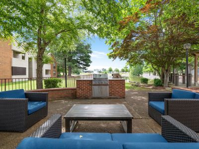 Outdoor resident lounge area with blue cushioned wicker seating next to a brick grilling station at Southcrest Lake Apartments in Southaven