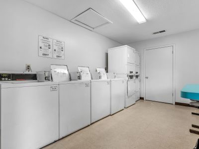 On-site community laundry room equipped with multiple white commercial washing machines and dryers at Southcrest Lake Apartments in Southaven