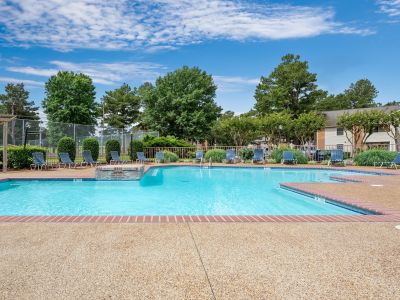 Wide view of the community swimming pool lined with blue lounge chairs and bordered by mature trees at Southcrest Lake Apartments in Southaven