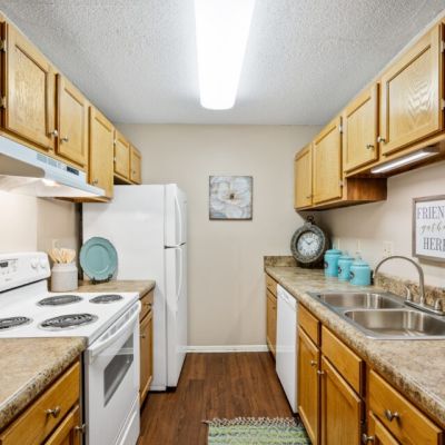 Galley kitchen featuring traditional oak cabinets, white appliances, and wood-style flooring at Southcrest Lake Apartments in Southaven