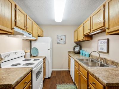 Galley kitchen featuring traditional oak cabinets, white appliances, and wood-style flooring at Southcrest Lake Apartments in Southaven