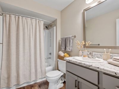 Modern bathroom with a granite-style vanity countertop, grey cabinetry, and a neutral shower curtain at The Ellington at Kirby apartments in Memphis