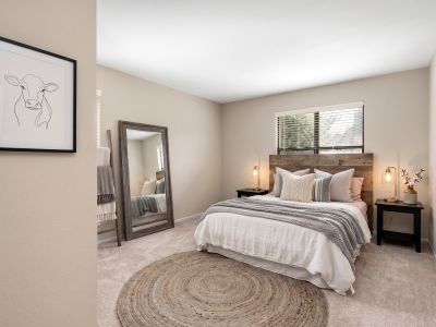 Virtually staged bedroom featuring a rustic wood headboard, a large floor mirror, and a braided rug at The Ellington at Kirby apartments in Memphis.