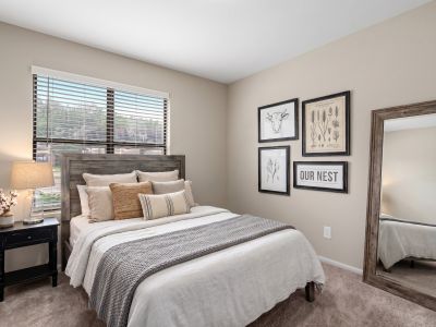 Staged bedroom layout showcasing neutral beige walls, a full-length mirror, and farmhouse-style wall art at The Ellington at Kirby apartments in Memphis.