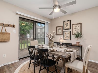 Virtually staged dining room with a wooden table, matching chairs, and a sliding glass door leading outside at The Ellington at Kirby apartments in Memphis.