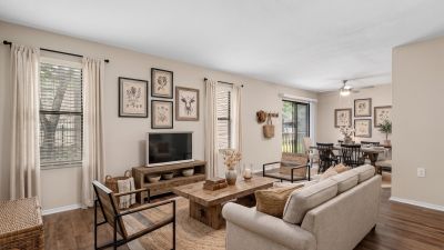 Staged living room with wood-look flooring, a cozy sofa, and an open layout leading to the dining area at The Ellington at Kirby apartments in Memphis.