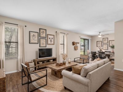 Staged living room with wood-look flooring, a cozy sofa, and an open layout leading to the dining area at The Ellington at Kirby apartments in Memphis.