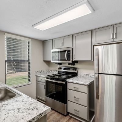 Galley kitchen equipped with stainless steel appliances, speckled granite-look counters, and grey cabinets at The Ellington at Kirby apartments in Memphis.