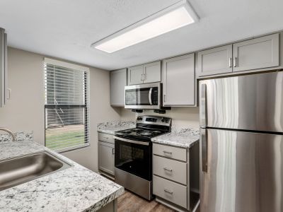 Galley kitchen equipped with stainless steel appliances, speckled granite-look counters, and grey cabinets at The Ellington at Kirby apartments in Memphis.