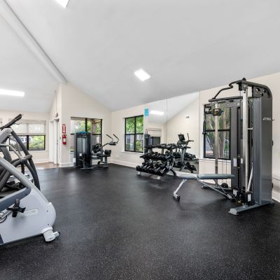 Fully equipped fitness space with cardio machines, a weight bench, and large wall mirrors at The Ellington at Kirby apartments in Memphis.