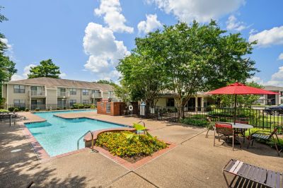 Sparkling outdoor swimming pool with a sun deck, patio tables, and red umbrellas at The Ellington at Kirby apartments in Memphis.