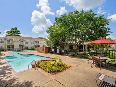 Sparkling outdoor swimming pool with a sun deck, patio tables, and red umbrellas at The Ellington at Kirby apartments in Memphis.