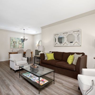 Open-concept living room styled with a brown sofa, cream armchairs, wood-style flooring, and a separate dining area at The Westbury apartments near Germantown.