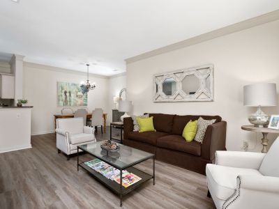 Open-concept living room styled with a brown sofa, cream armchairs, wood-style flooring, and a separate dining area at The Westbury apartments near Germantown.