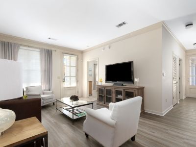 Main living area highlighting neutral beige walls, crown molding, wood-look vinyl plank flooring, and a television on a wooden media console at The Westbury apartments near Germantown.
