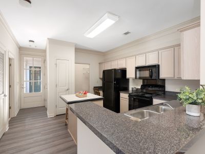 Apartment kitchen with dark granite-look countertops, light-colored cabinetry, black appliances, a small central island, and wood-look flooring at The Westbury apartments near Germantown.