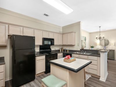 Modern apartment kitchen featuring a center island with a tiled top, light wood cabinetry, black appliances, and a breakfast bar overlooking the dining room at The Westbury apartments near Germantown.
