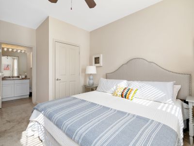 Master bedroom interior featuring a tufted fabric headboard, neutral walls, and a doorway leading into the ensuite bathroom at The Westbury apartments near Germantown.