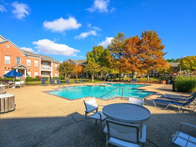 Resident pool deck featuring patio tables, chairs, and blue umbrellas next to the brick residential buildings at The Westbury apartments near Germantown.