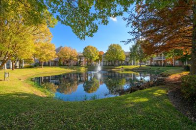Shaded walking paths framing a central community pond with a water fountain and vibrant seasonal trees at The Westbury apartments near Germantown.