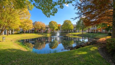 Shaded walking paths framing a central community pond with a water fountain and vibrant seasonal trees at The Westbury apartments near Germantown.