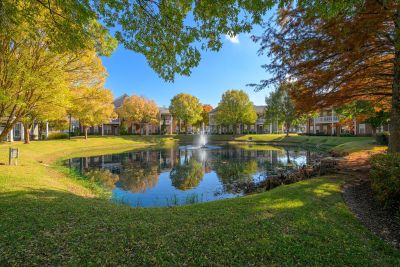 Shaded walking paths framing a central community pond with a water fountain and vibrant seasonal trees at The Westbury apartments near Germantown.